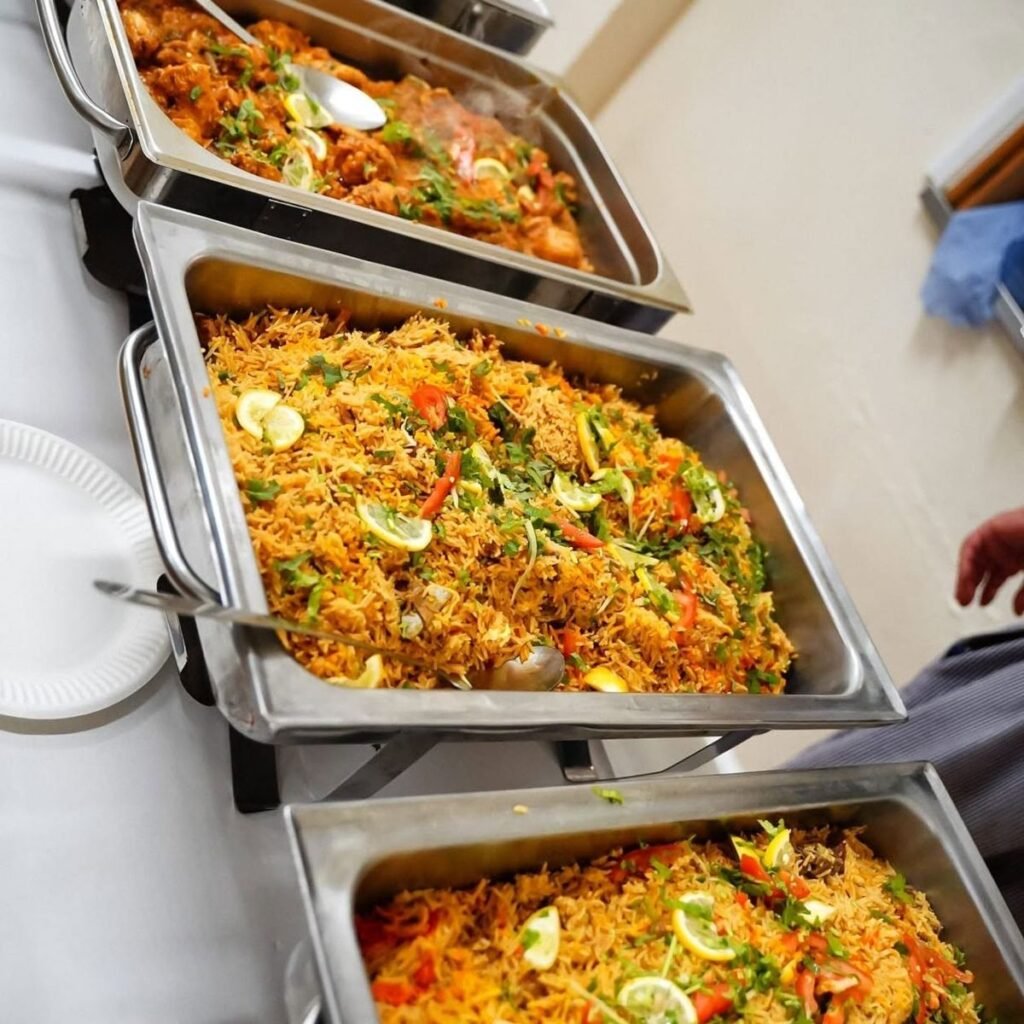 Steel chafing trays of yellow rice biryani with lemon slices and herbs at a buffet