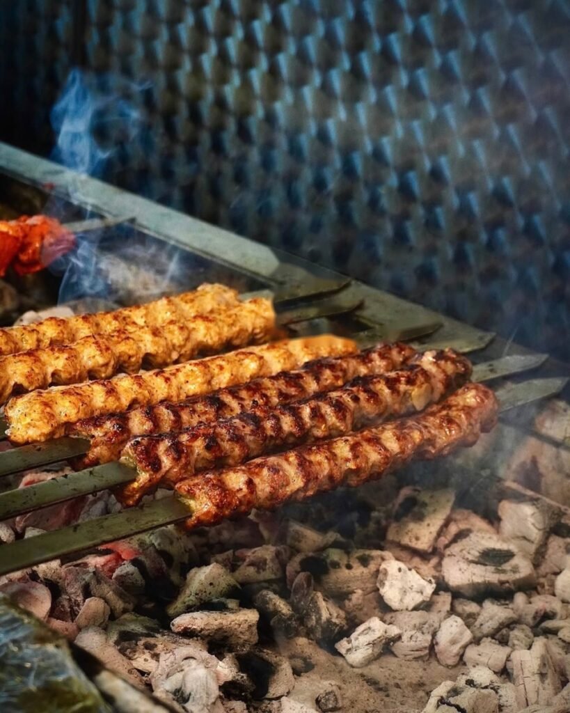 Seekh kebabs on skewers grilling over charcoal with smoke rising