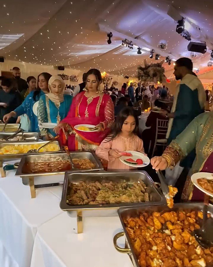 Guests in traditional dress serving themselves from a hot buffet line at a catered celebration