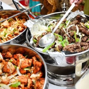Steel chafing dishes of spiced meat with peppers and onions and chicken tikka at a buffet